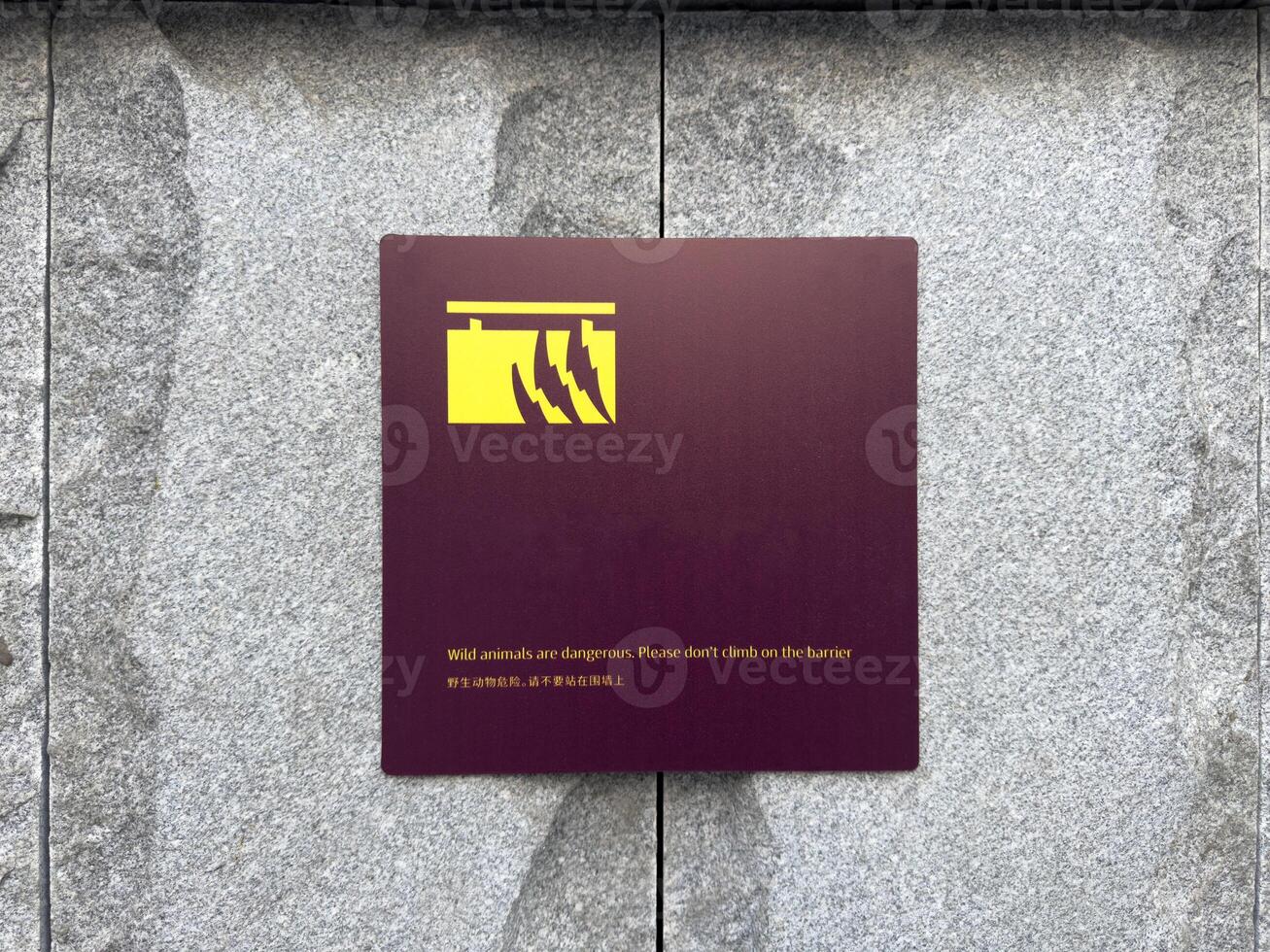 Warning sign with minimalist graphic of claws mounted on stone wall, cautioning visitors against climbing over barrier in area with wild animals, combining safety message with clean modern design photo