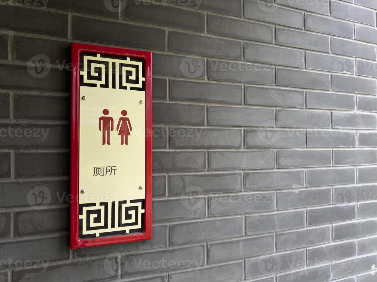 Restroom sign in Chinese style with traditional patterns and red accents, mounted on a gray brick wall. The sign includes male and female pictograms and Chinese characters indicating public toilet photo