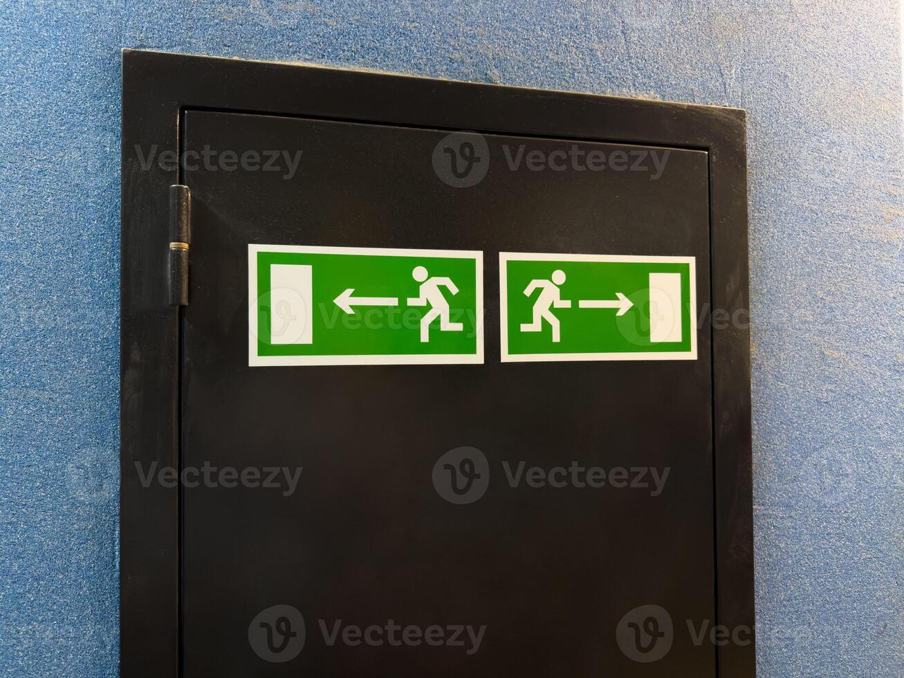 Minimalist composition with two symmetrical emergency exit signs on black panel against blue wall, combining graphic clarity and functional interior detail in modern public space or institution photo