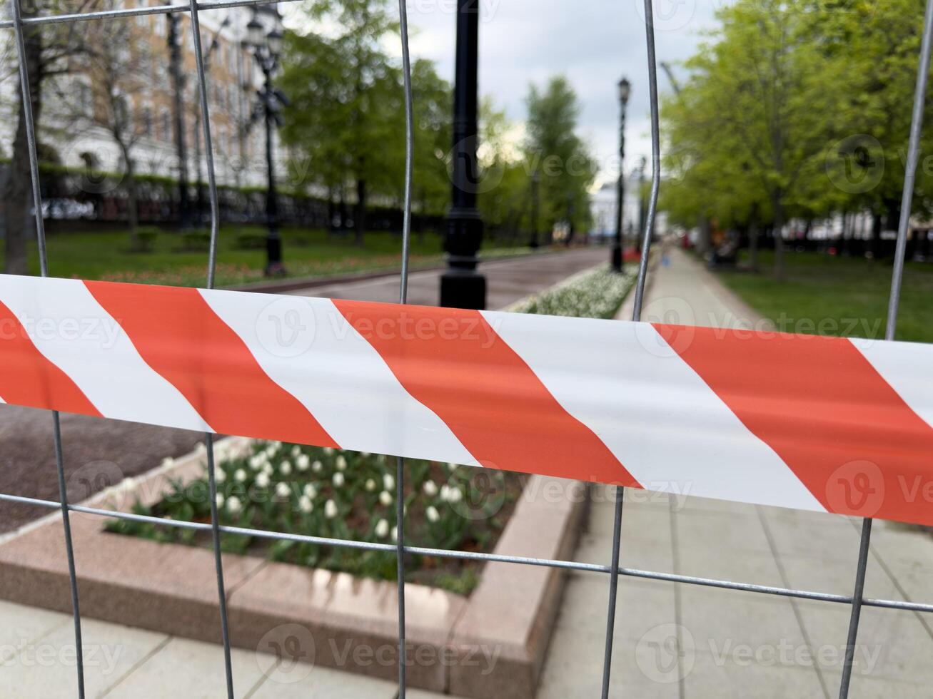 Warning tape on metal fence blocks access to landscaped park area during maintenance, symbolizing safety, restricted entry, and temporary closure for improvement works photo