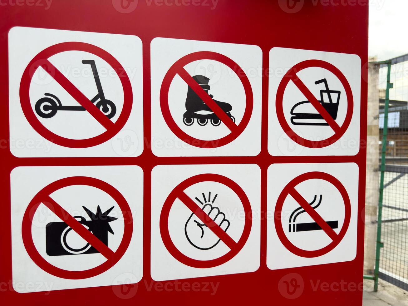 Closeup of red prohibition signboard with six warning icons indicating no scooters, rollerblades, bumper cars, flash photography, loud noises, or smoking in restricted area near entrance photo