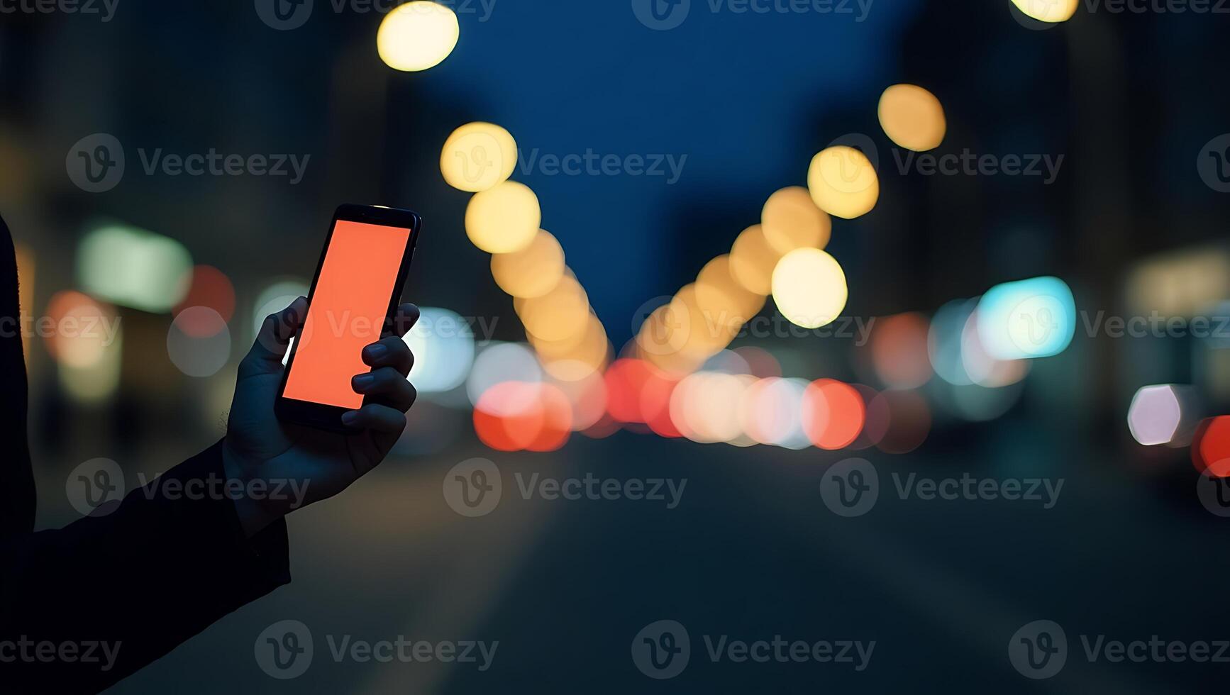 Hand holding smartphone with orange screen at night in city with bokeh lights photo