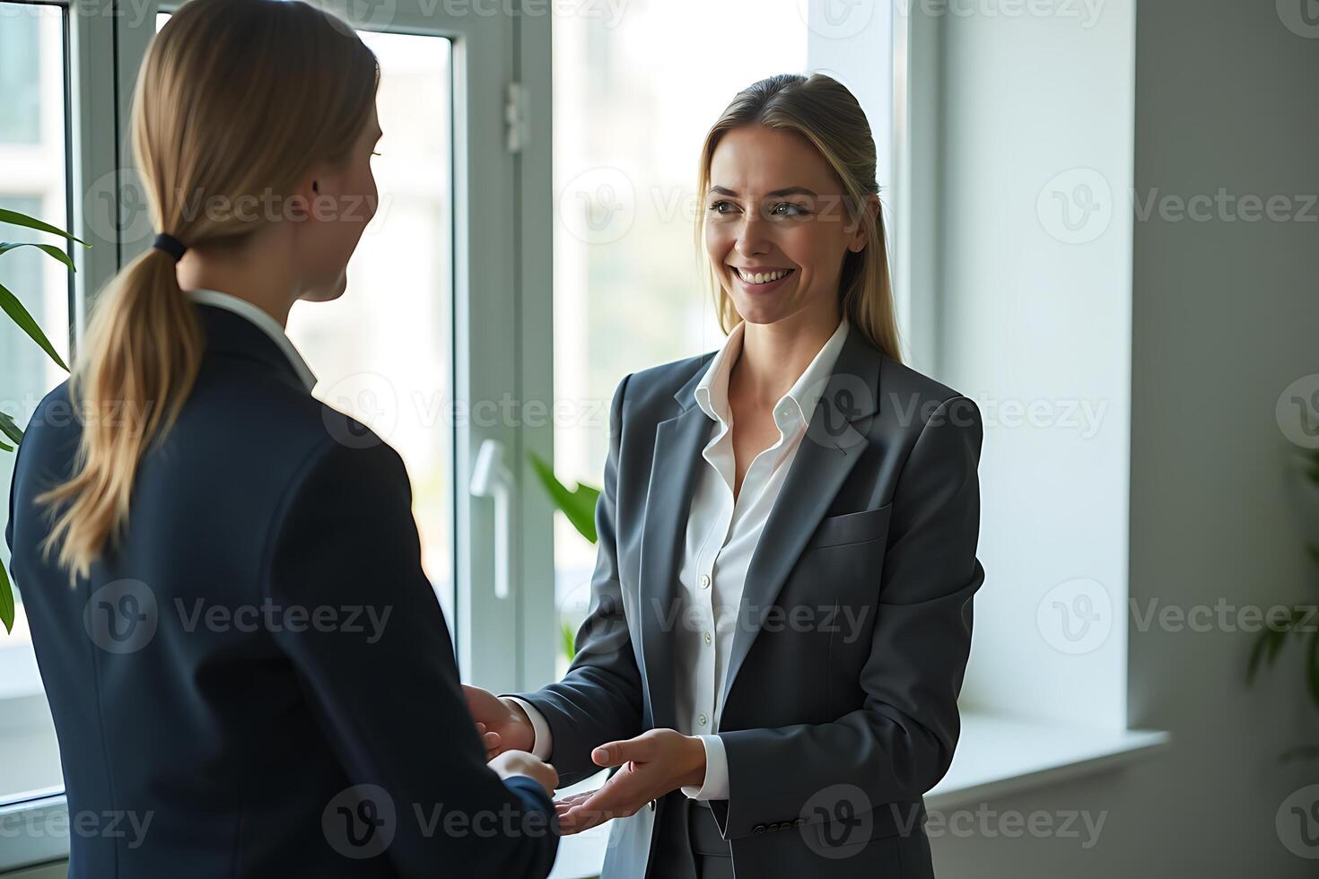 Two businesswomen in suits shaking hands smiling in a well lit professional environment photo