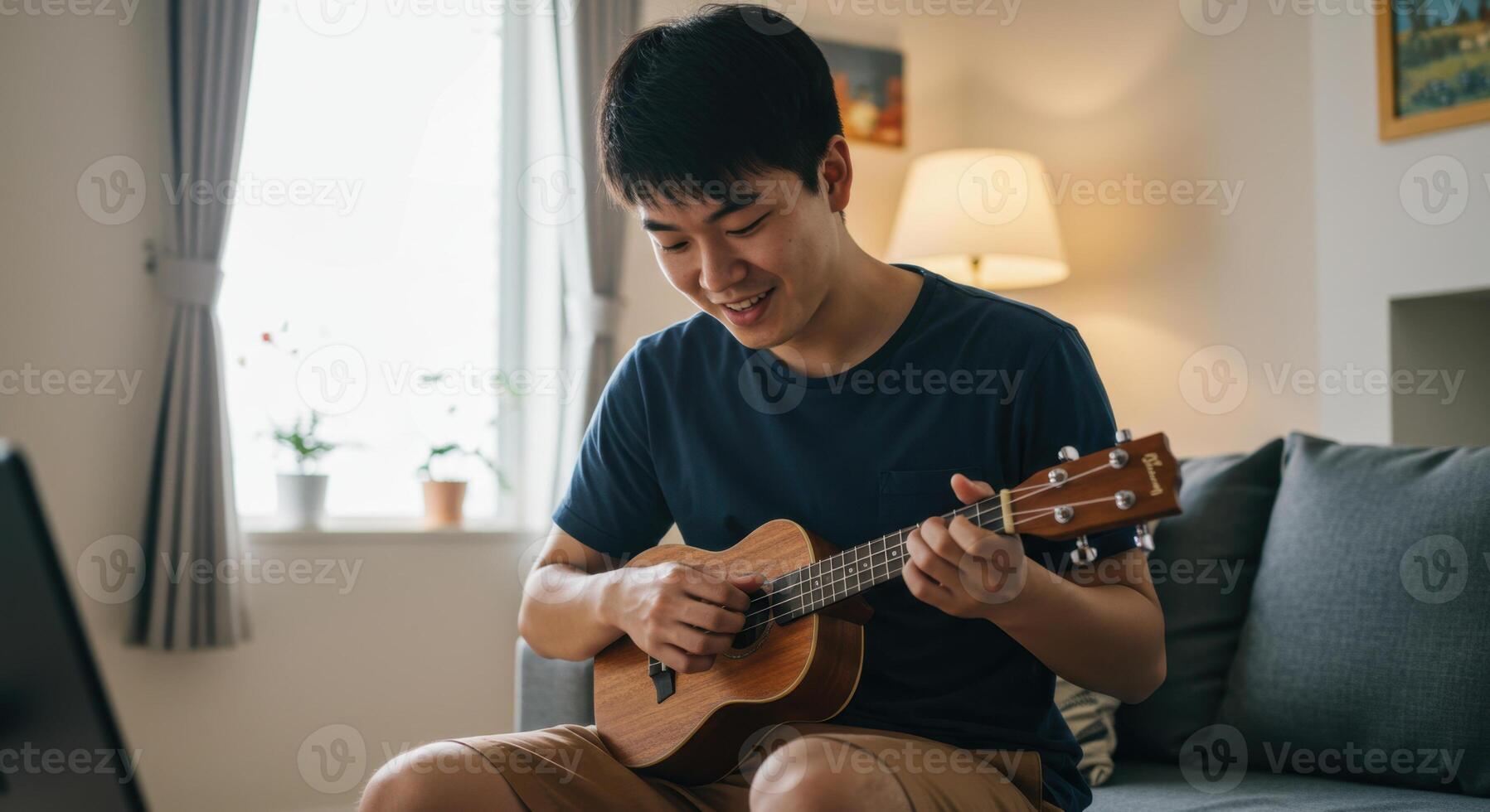 Smiling Asian Man Playing Ukulele at Home in a Relaxed Living Room Setting photo