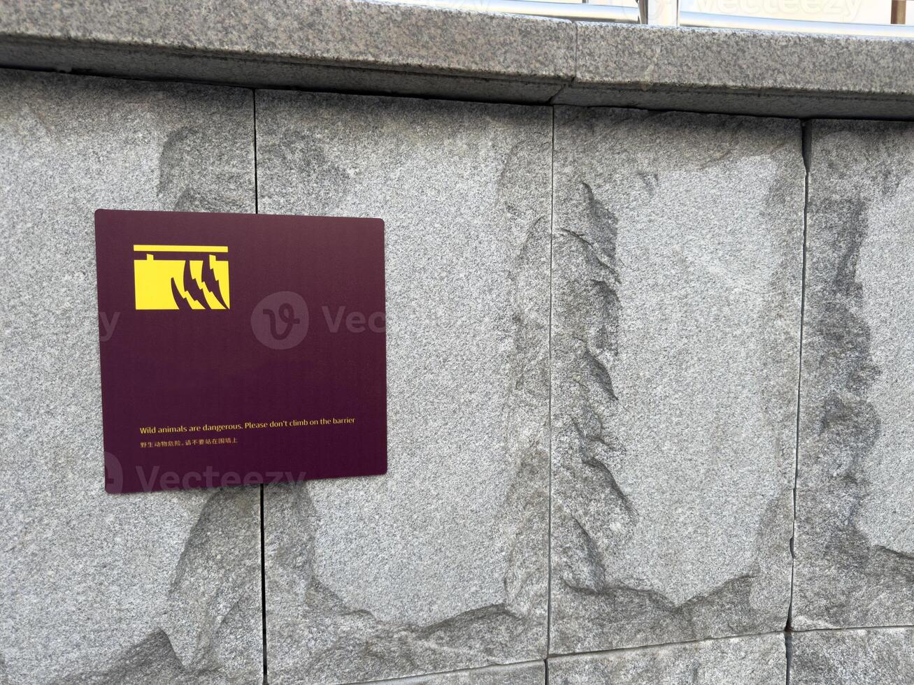 Safety sign on stone wall warns visitors not to climb over barrier in area with wild animals, emphasizing responsible behavior and risk prevention in zoological parks or wildlife enclosures photo