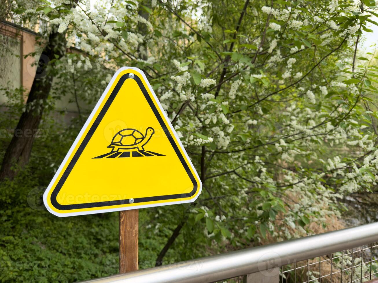 Bright yellow triangular warning sign with turtle icon stands in green park zone, serving as clear visual symbol in public space, combining environmental education with modern graphic design photo