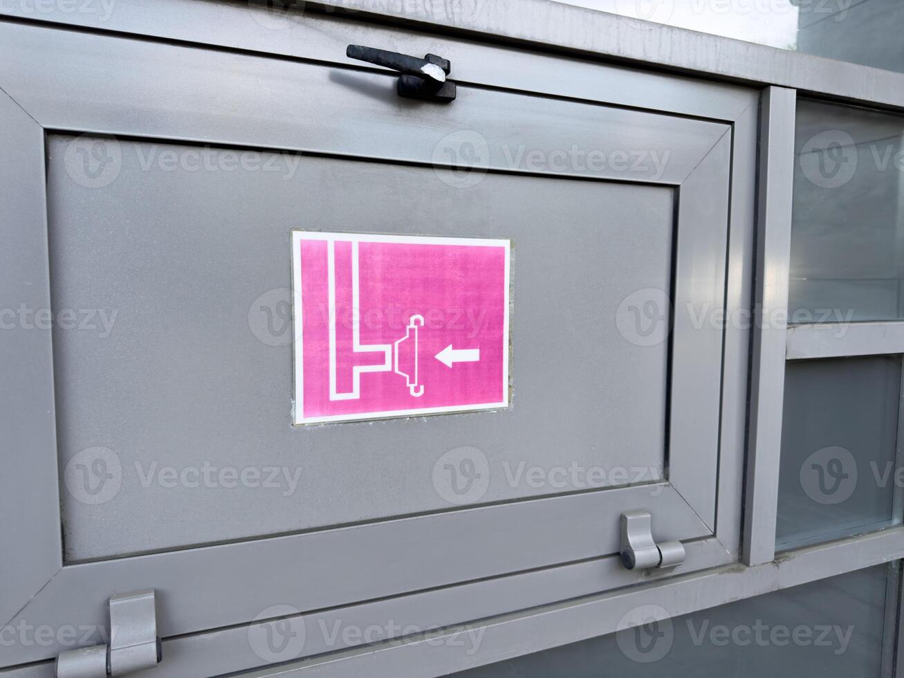 Close up of gray metal cabinet with pink fire hose reel sign showing schematic icon and directional arrow, part of exterior fire safety system installed on public or commercial building facade photo