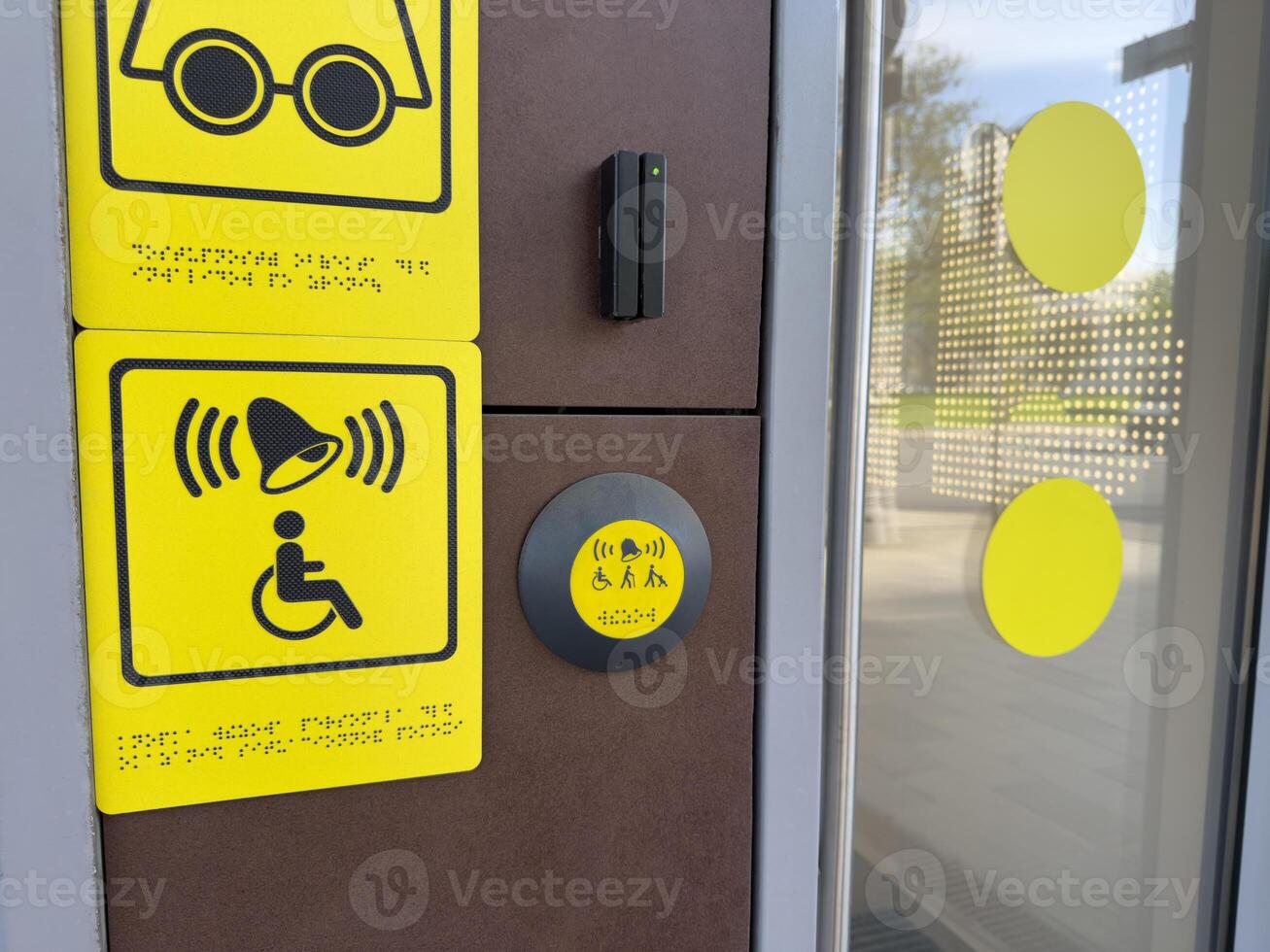Accessibility call system with yellow tactile and audio symbols, including Braille text and assistance button near glass door, designed to support people with disabilities in modern infrastructure photo