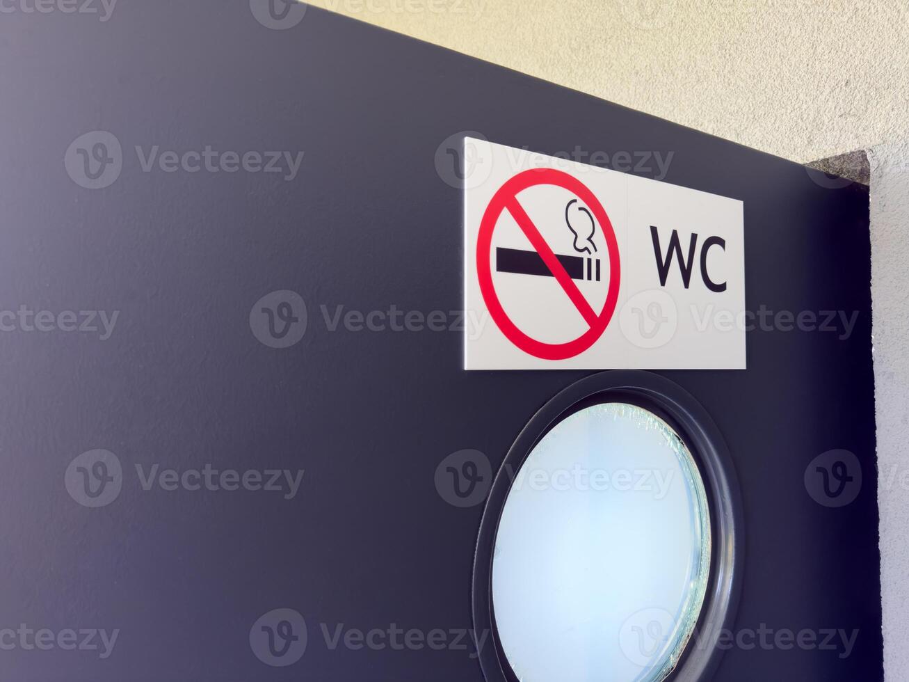 Closeup of WC door with round frosted window and no smoking sign on white label, showing clear visual message for public restroom users in clean and modern architectural setting photo