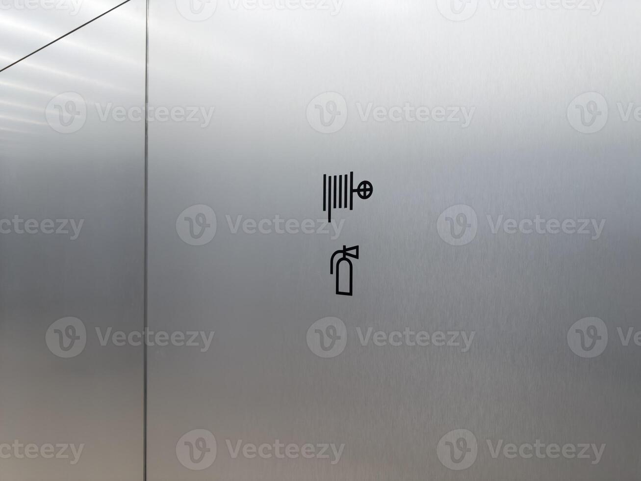 Minimal fire safety sign on metal wall. Black icon indicates location of fire hose and extinguisher. Emergency protection in public building or office interior photo