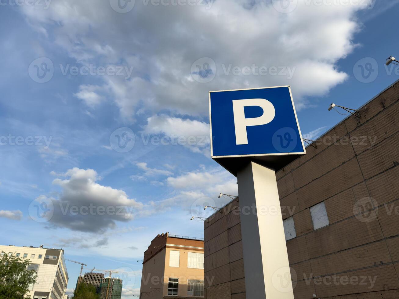 Large, bold blue P parking sign stands tall in the foreground of an industrial style urban building, framed by dramatic sky and scattered clouds, highlighting the practical side of city architecture photo