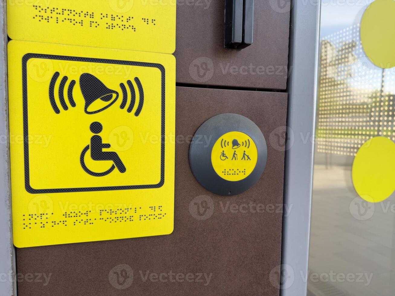 Yellow tactile signage and assistance button with bell and disability symbols including Braille, providing accessible user interface near modern entrance for inclusive and barrier free access photo