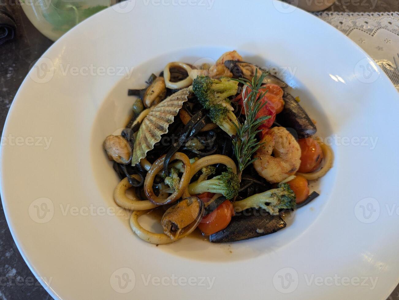 Black pasta with seafood and baked vegetables on a white plate. Close-up photo