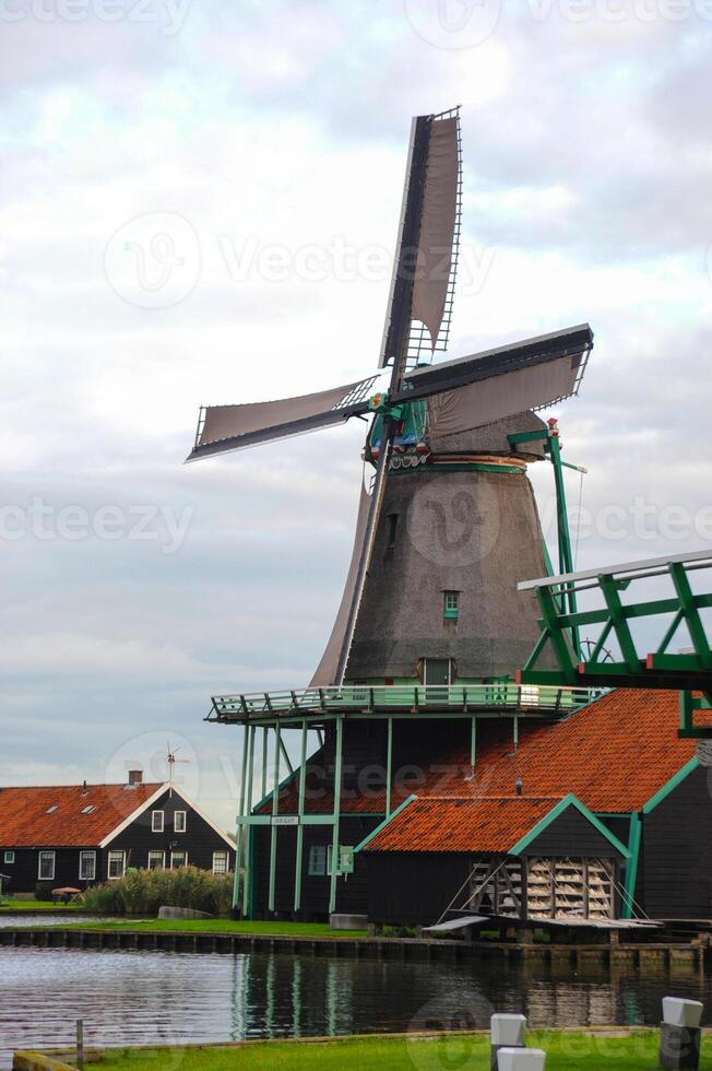 Dutch countryside featuring classic wooden buildings and a windmill on a river. photo