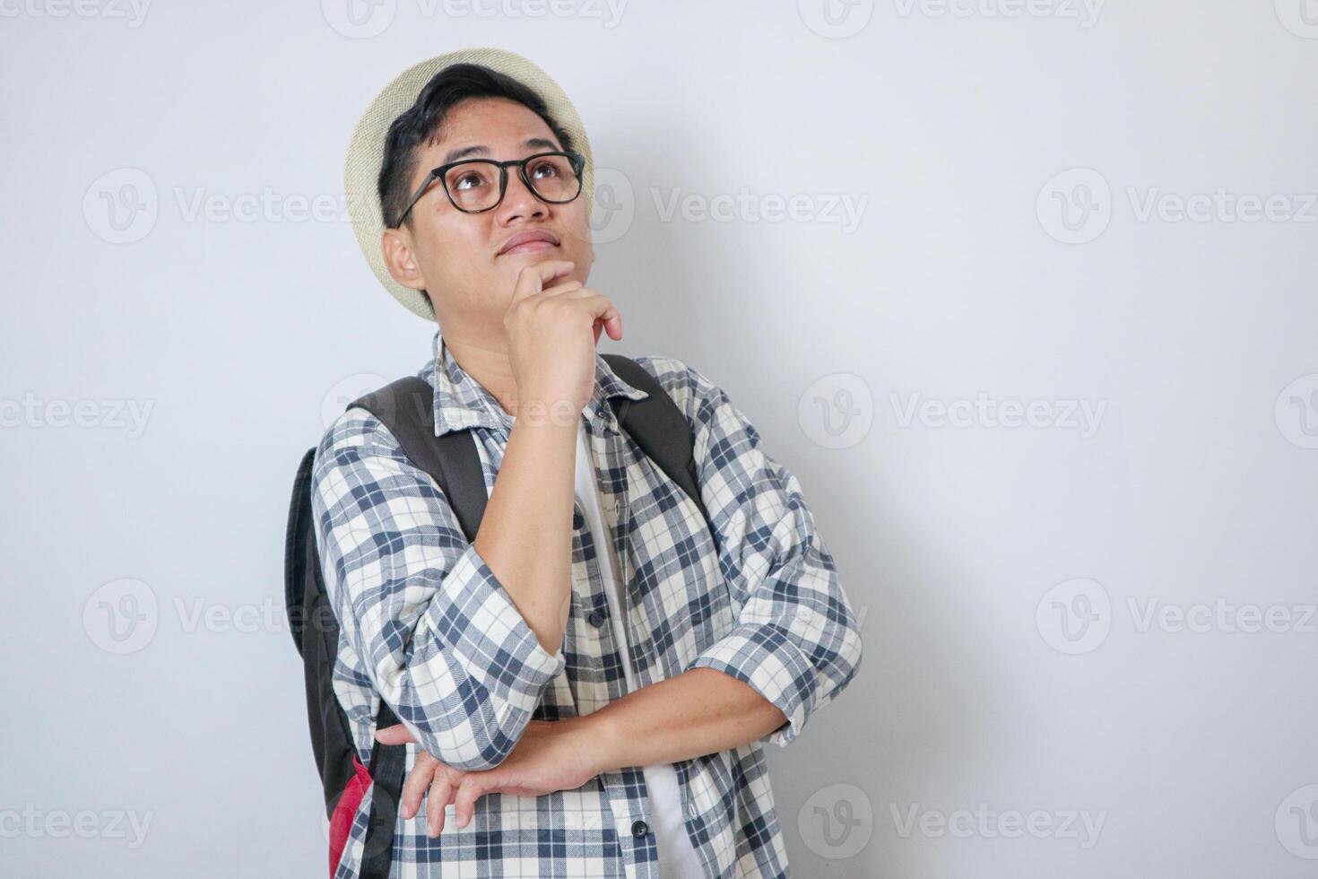 Thoughtful asian adult man tourist standing while looking above. Concept of travel. Isolated on white background photo