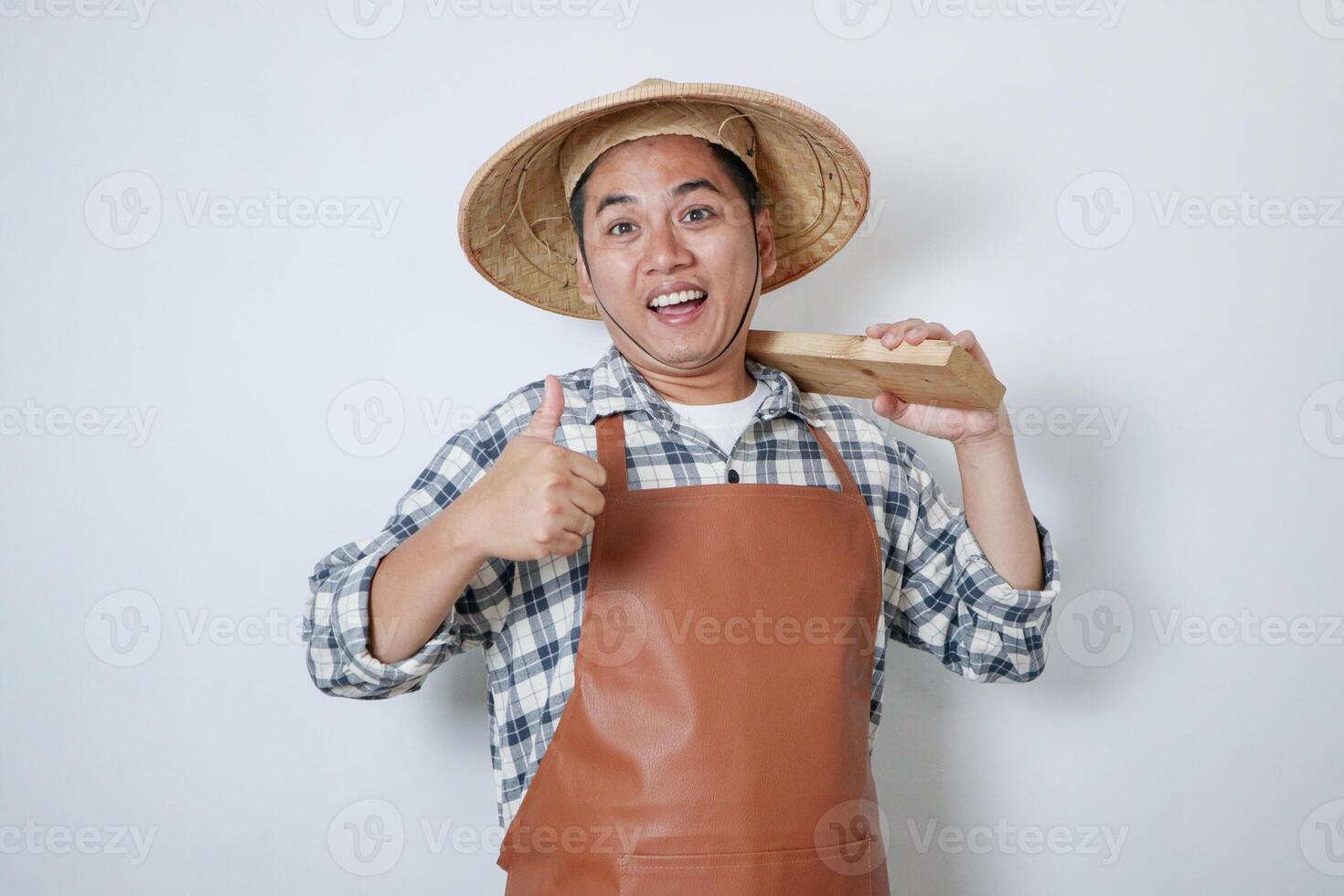 Happy Asian farmer wearing farmer shirt and Caping carrying a Pacul isolated on white background. Human gestures concept photo