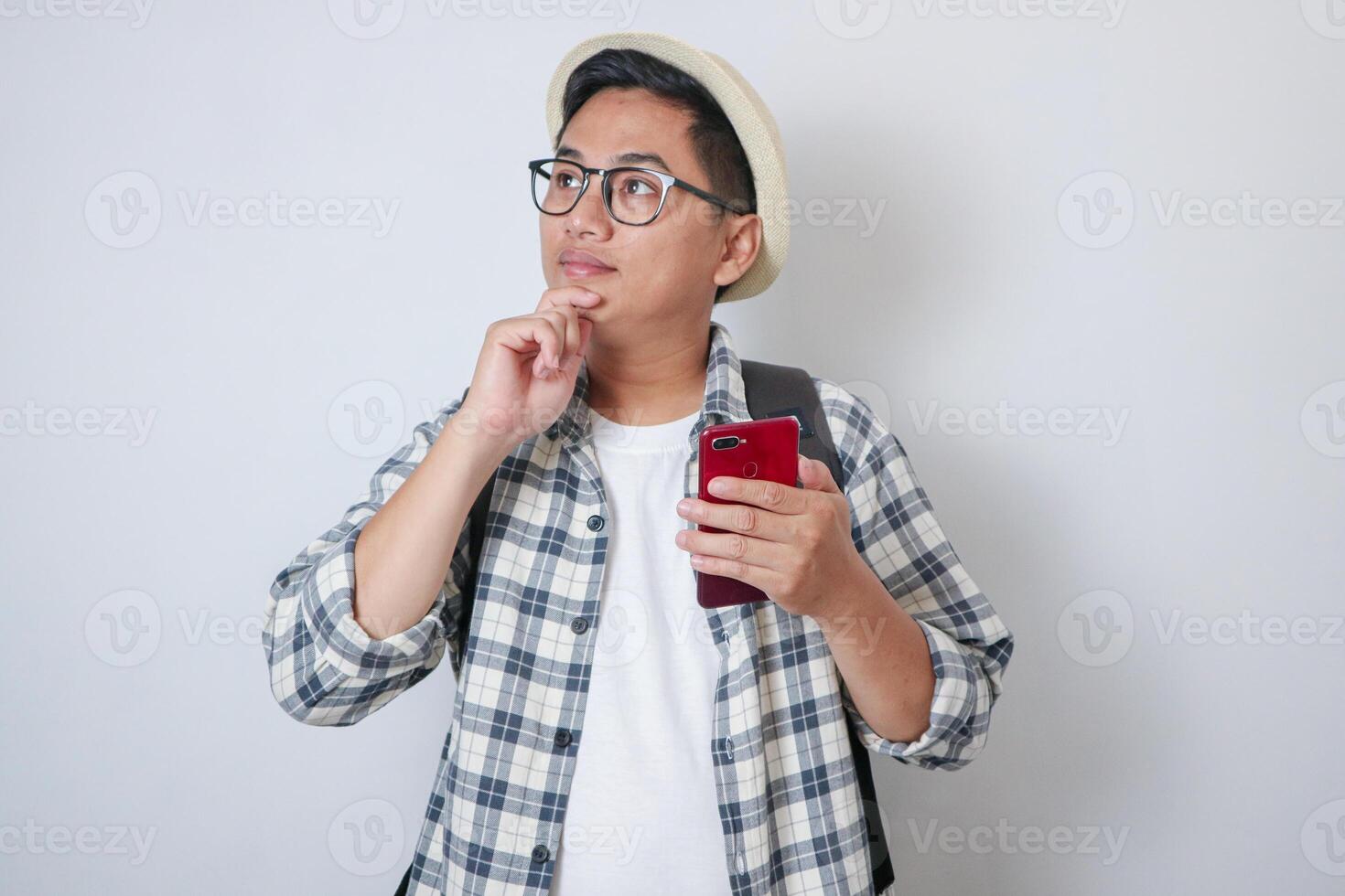 Doubtfully Young Asian Hikers Man Using Phone While Thinking With Hand On Chin Isolated On white Background photo