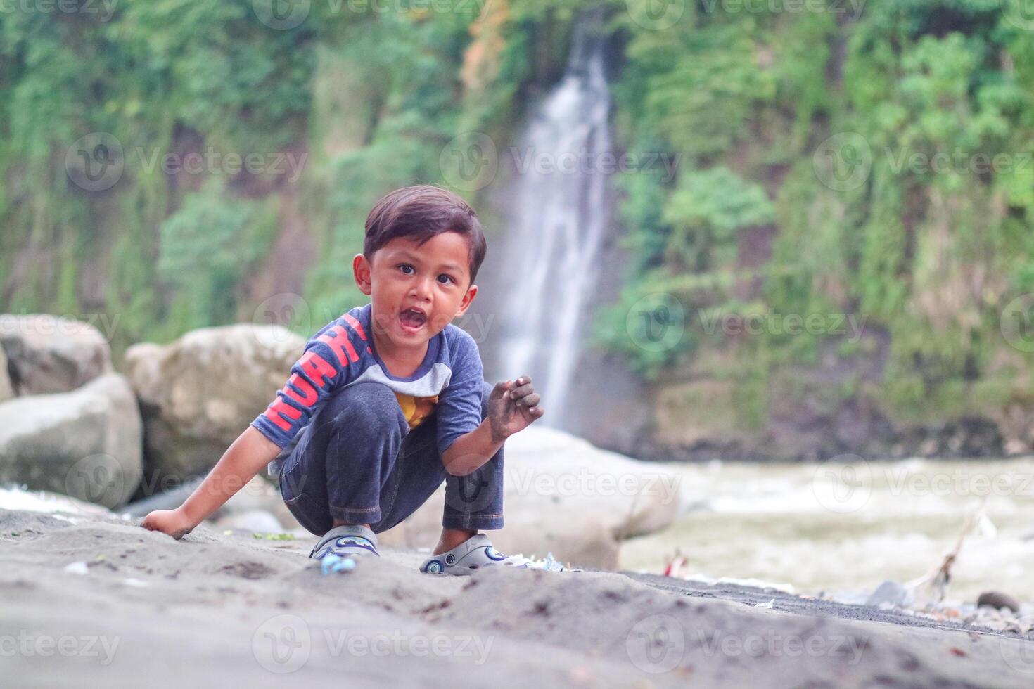 Asian children cute or kid boy smile with fun and enjoy playing with show smile for take a photo on waterfall with stone or rock and holiday relax trip for summer at waterfall