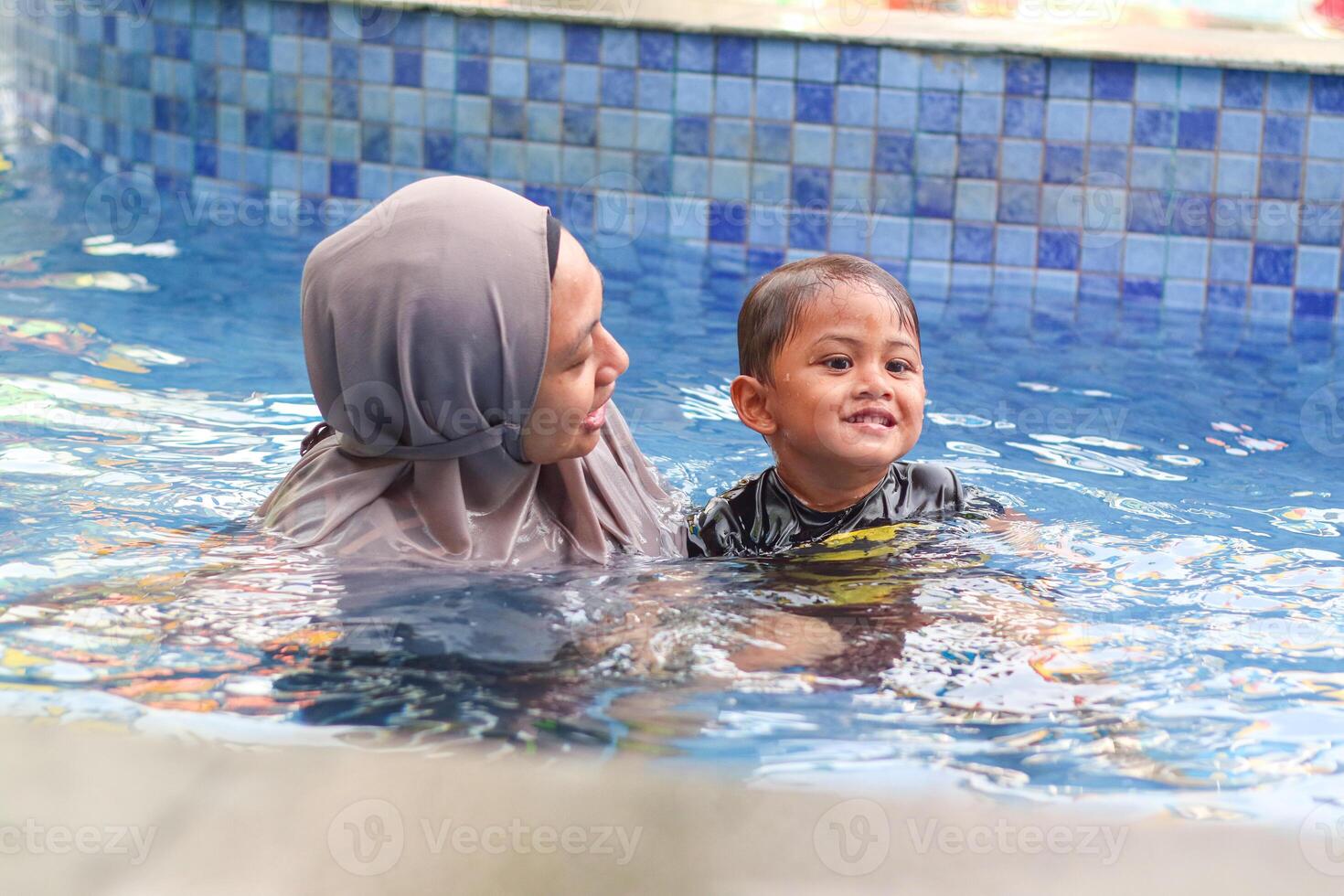 Cute boy with his mother playing in a pool of water during the summer photo