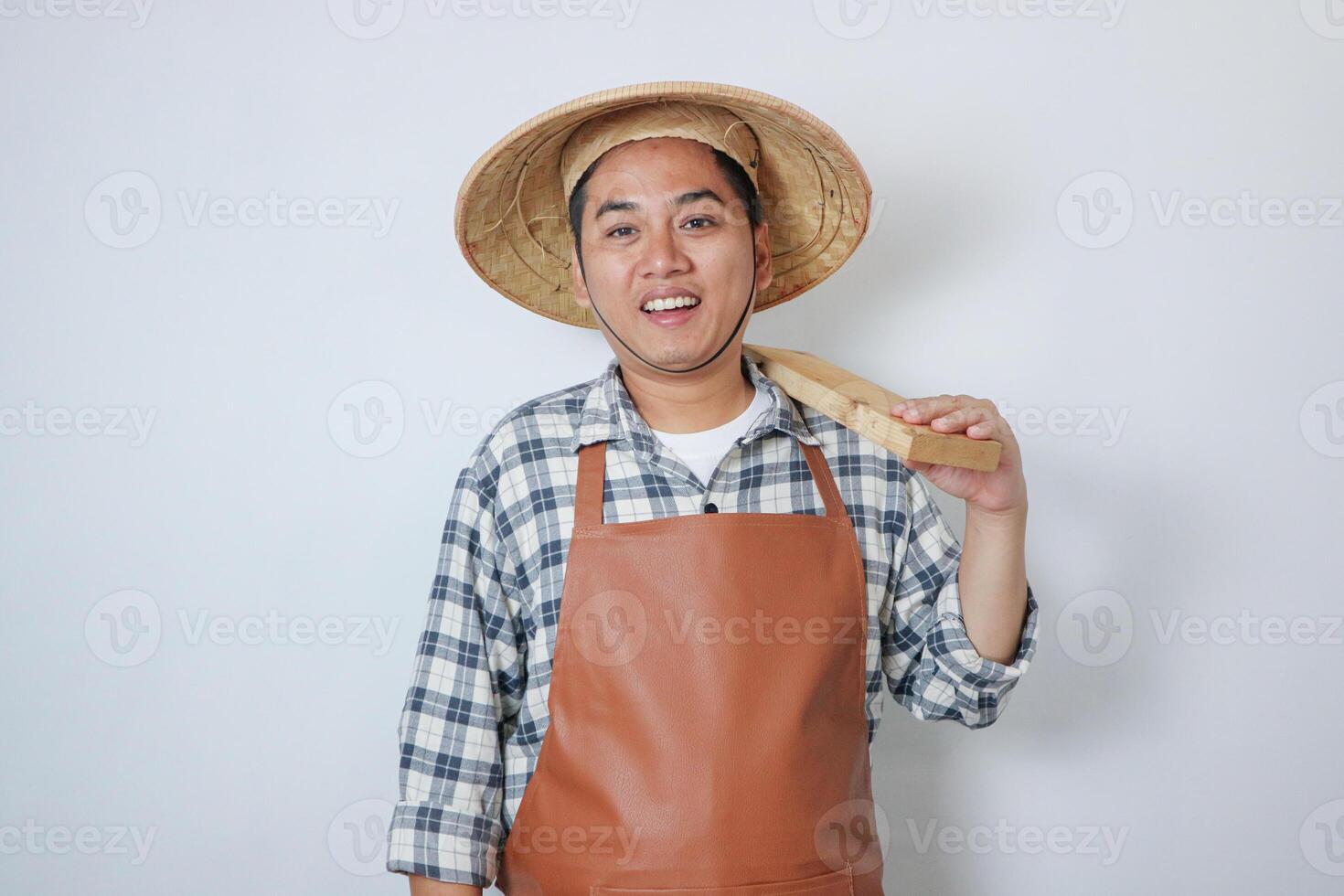 Young asian man wearing farmer hat showing happy face expression while his hand holding tool something photo