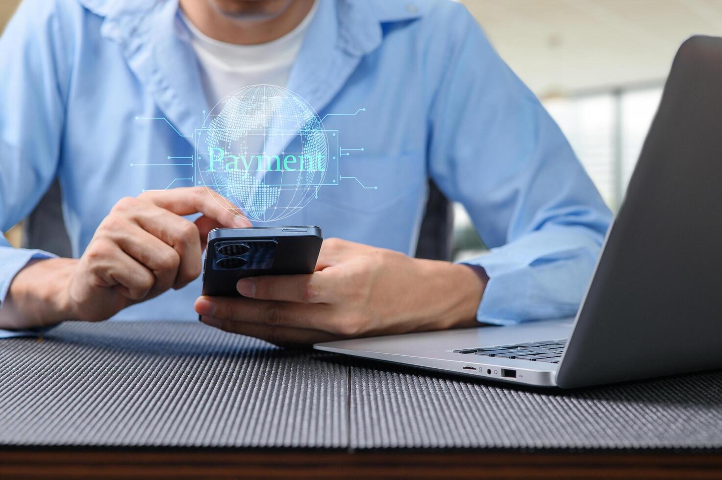 Man Using Smartphone for Digital Payment with Laptop in Background photo