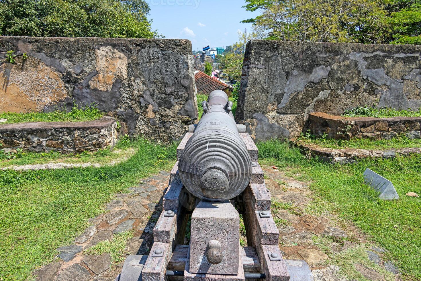 Old cannon at Galle Fort pointing toward the ocean under blue sky and palm trees 6 photo