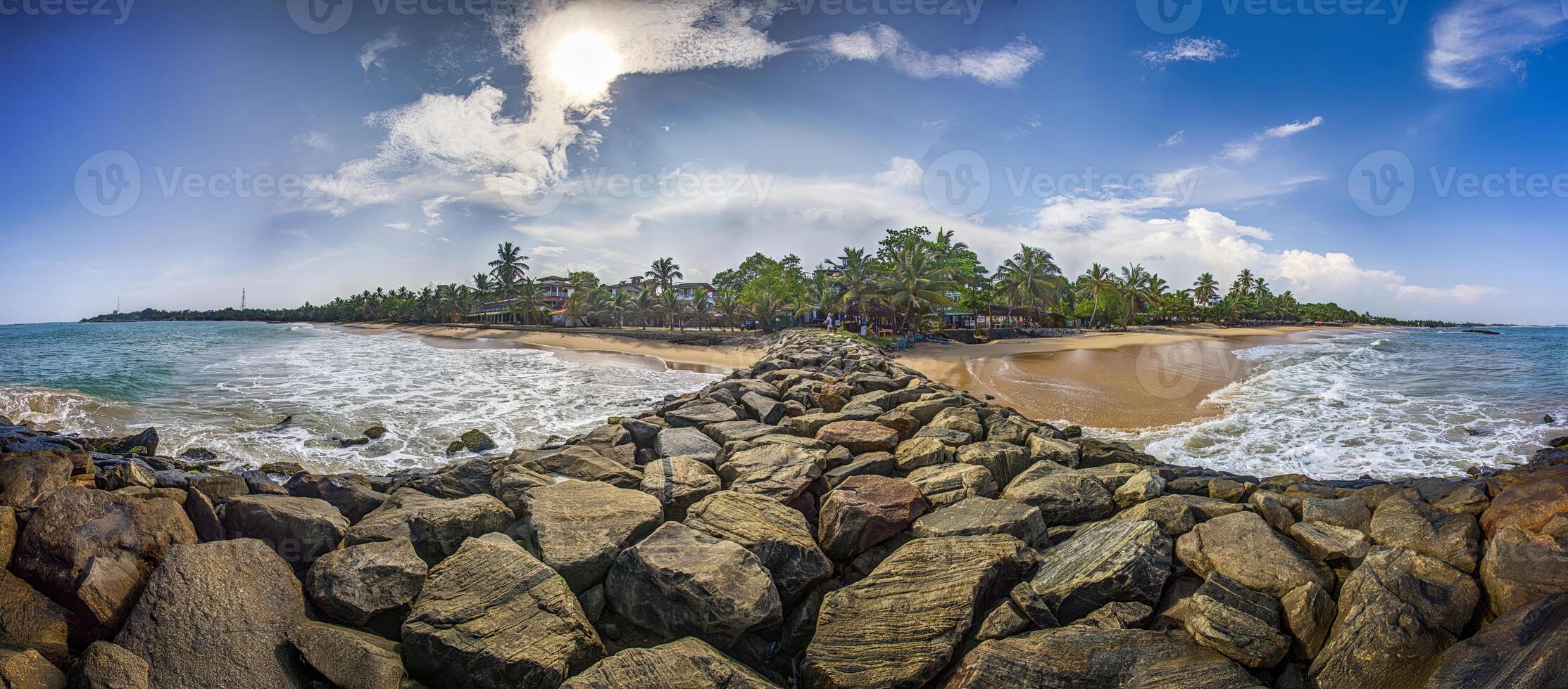 Rocky jetty at sunny Tangalle beach with palm trees and ocean waves photo