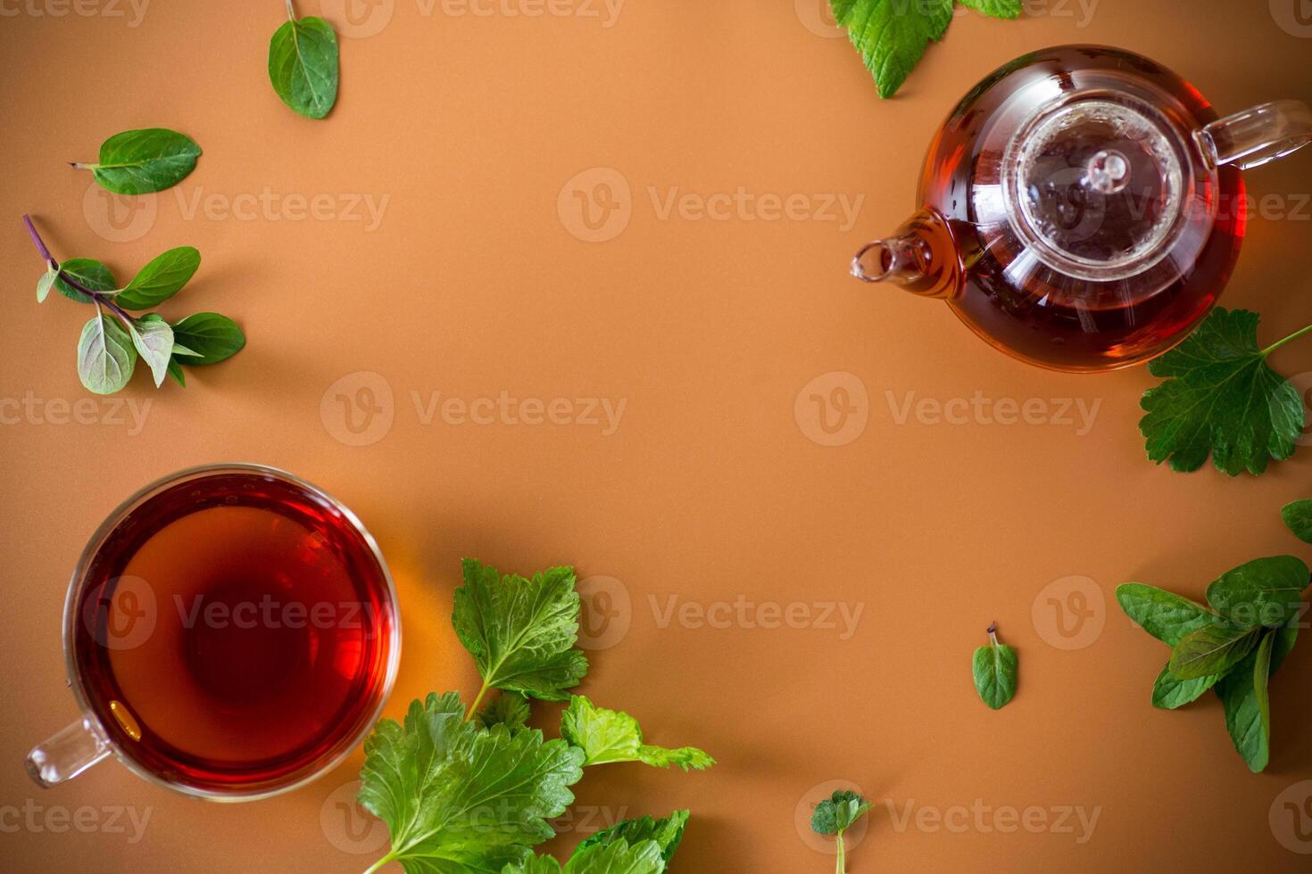 Green tea with currant leaves and mint in glass teapot and cup on brown background. Top view photo