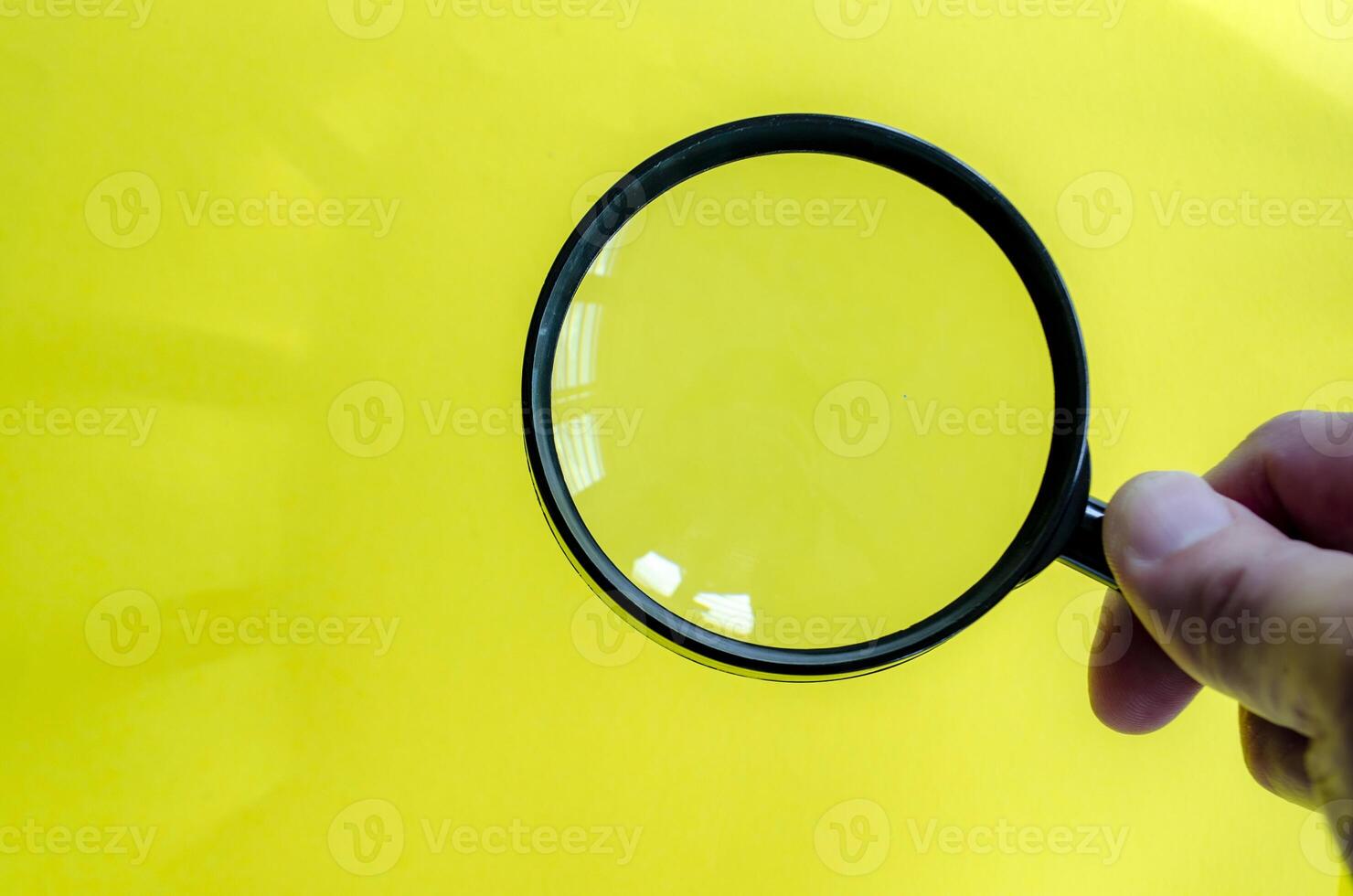 Hand holding a magnifying glass against a bright yellow background. Searching, examining, focusing or investigation concept. photo