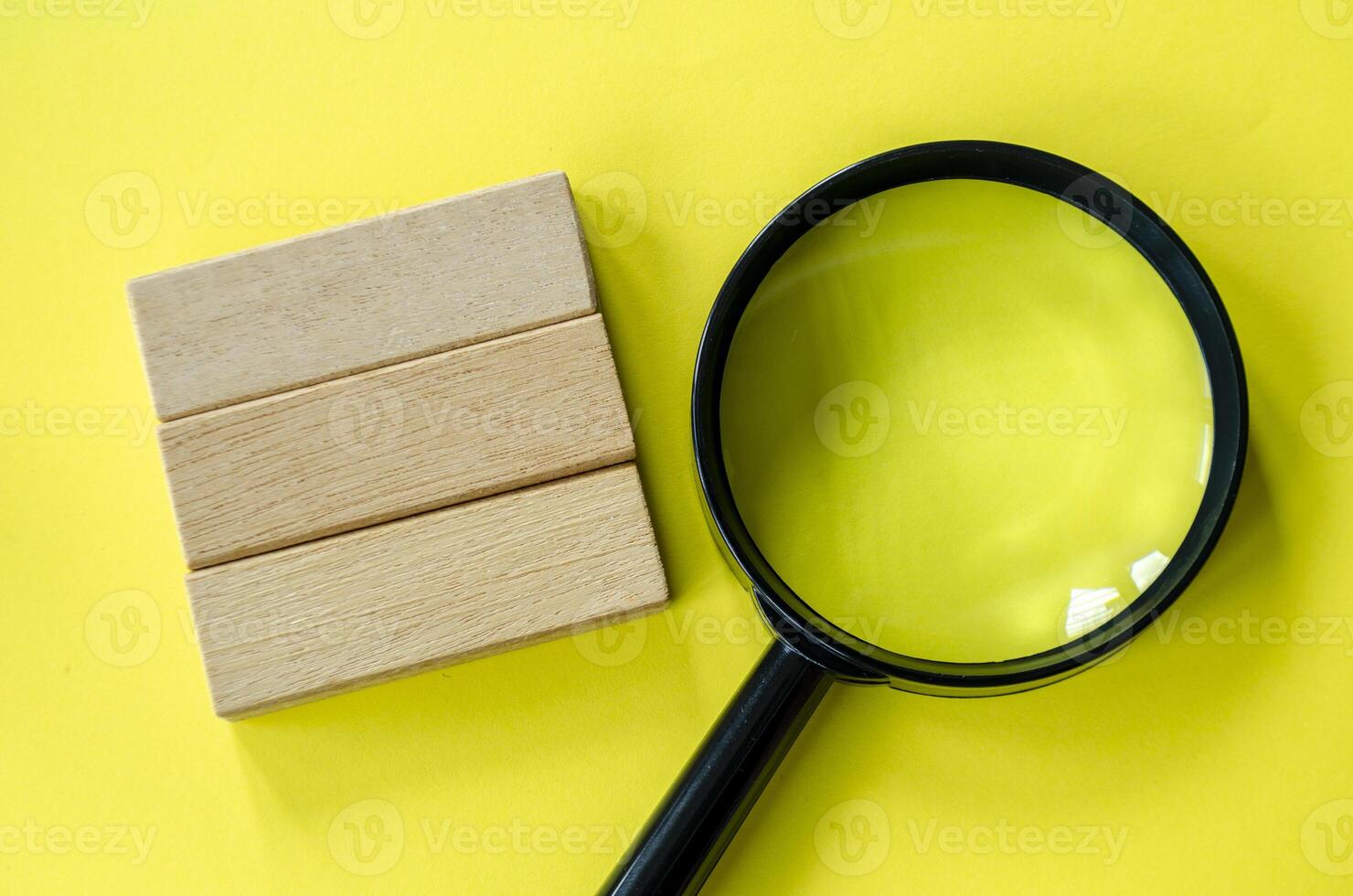 Magnifying glass against a bright yellow background with customizable space on wooden block for text photo