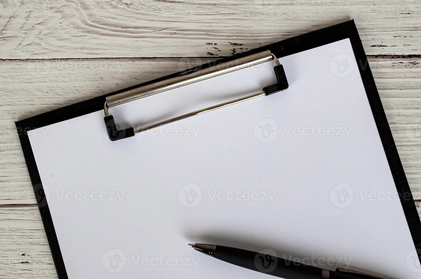 Top view of a blank clipboard with a sheet of white paper and a black pen. Copy space concept photo