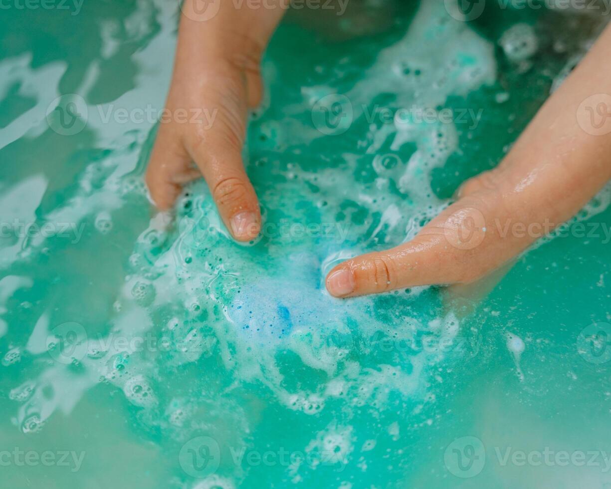 Close-up of babys hands playing with soap in water, soapy small and big bubbles in turquoise water, in the bathtub, in the sea. photo