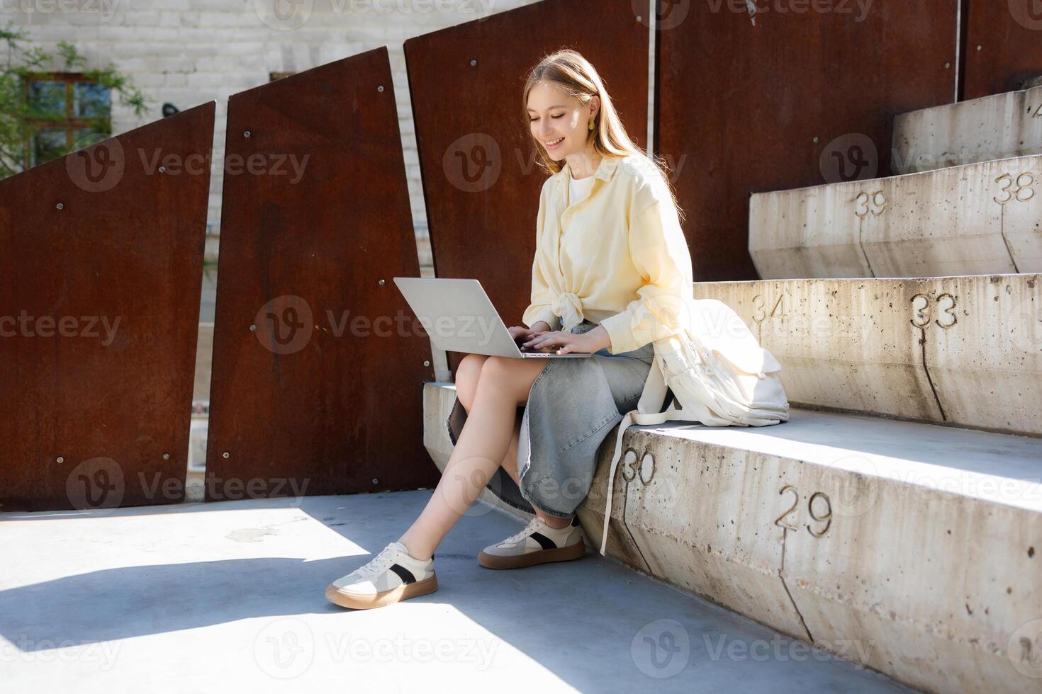 Young woman working on laptop while sitting on outdoor steps in an urban setting during daylight hours photo