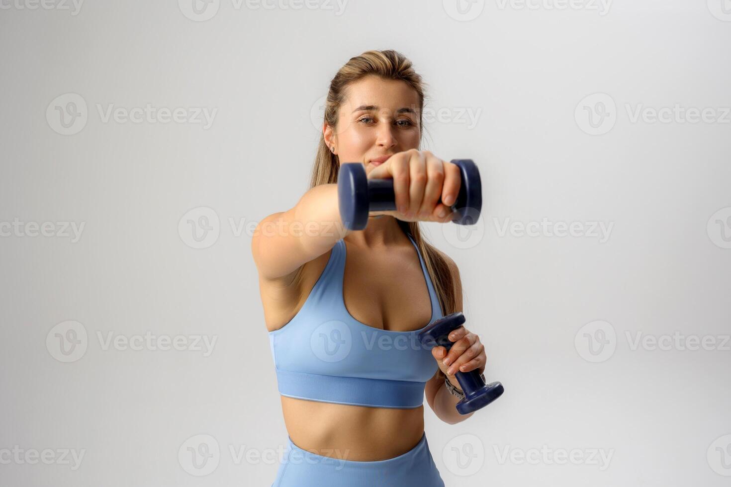 Female athlete demonstrating strength training with dumbbells in a bright studio setting during an indoor workout session photo