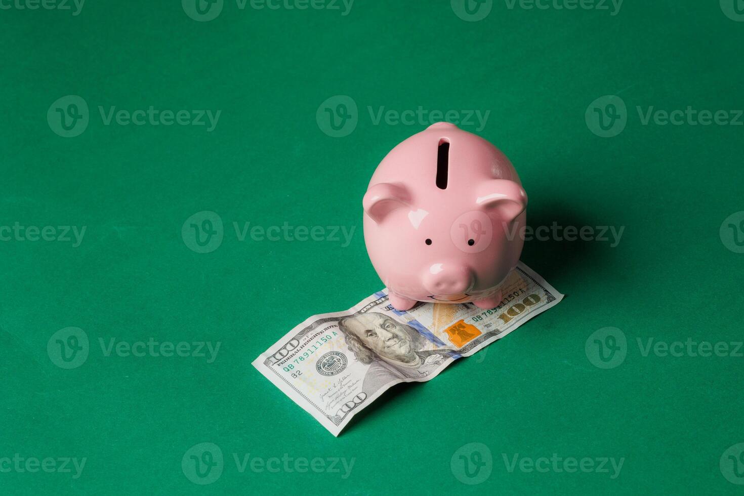 Savings grow as a pink piggy bank sits on a hundred dollar bill on a green background photo