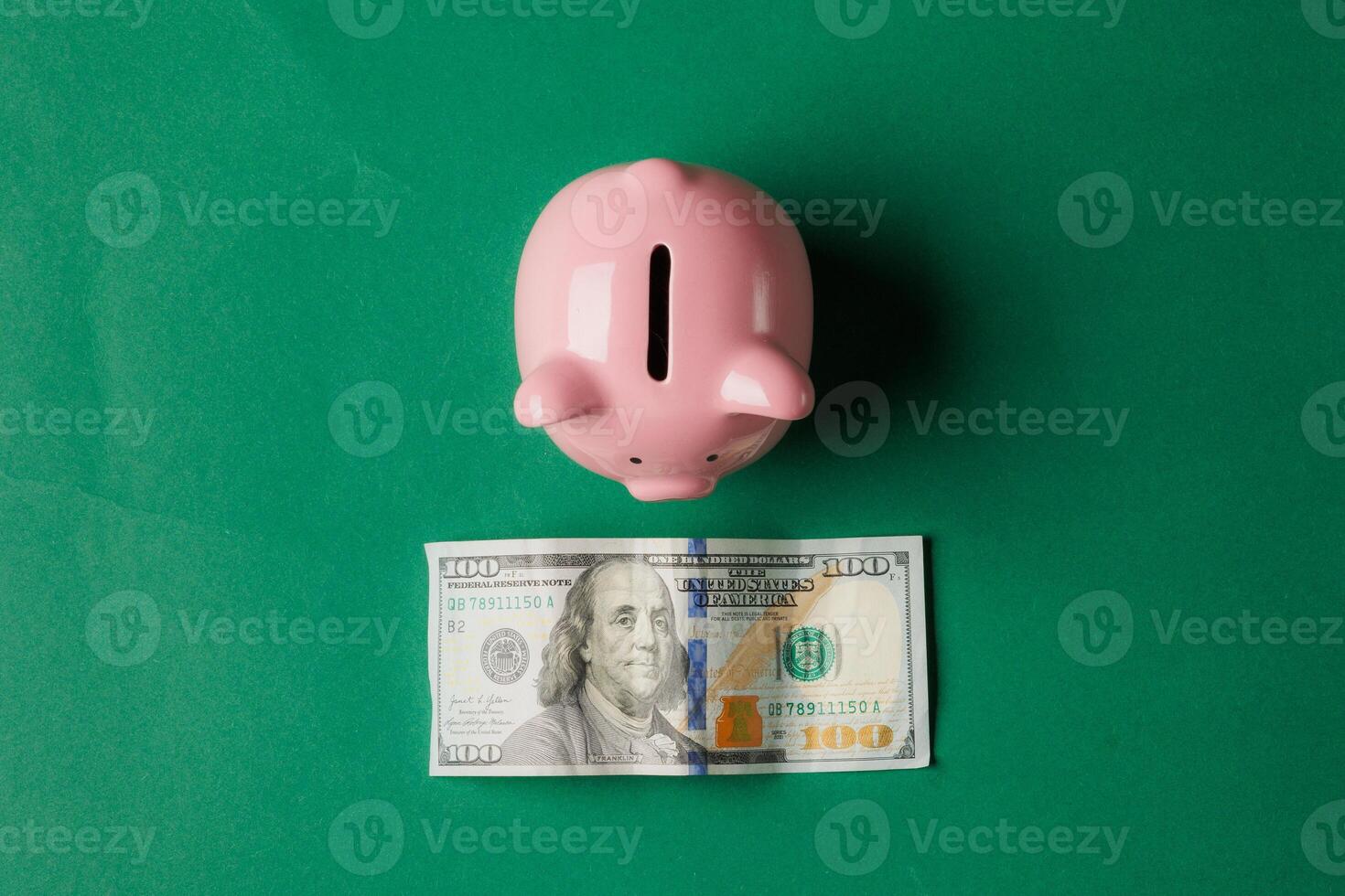 Saving money with a pink piggy bank and a hundred dollar bill on a green background photo