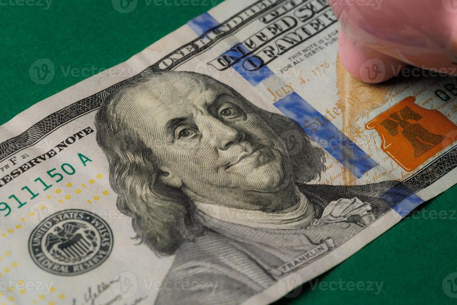 Close-up of a United States hundred dollar bill featuring Benjamin Franklin and a piggy bank on a green background photo