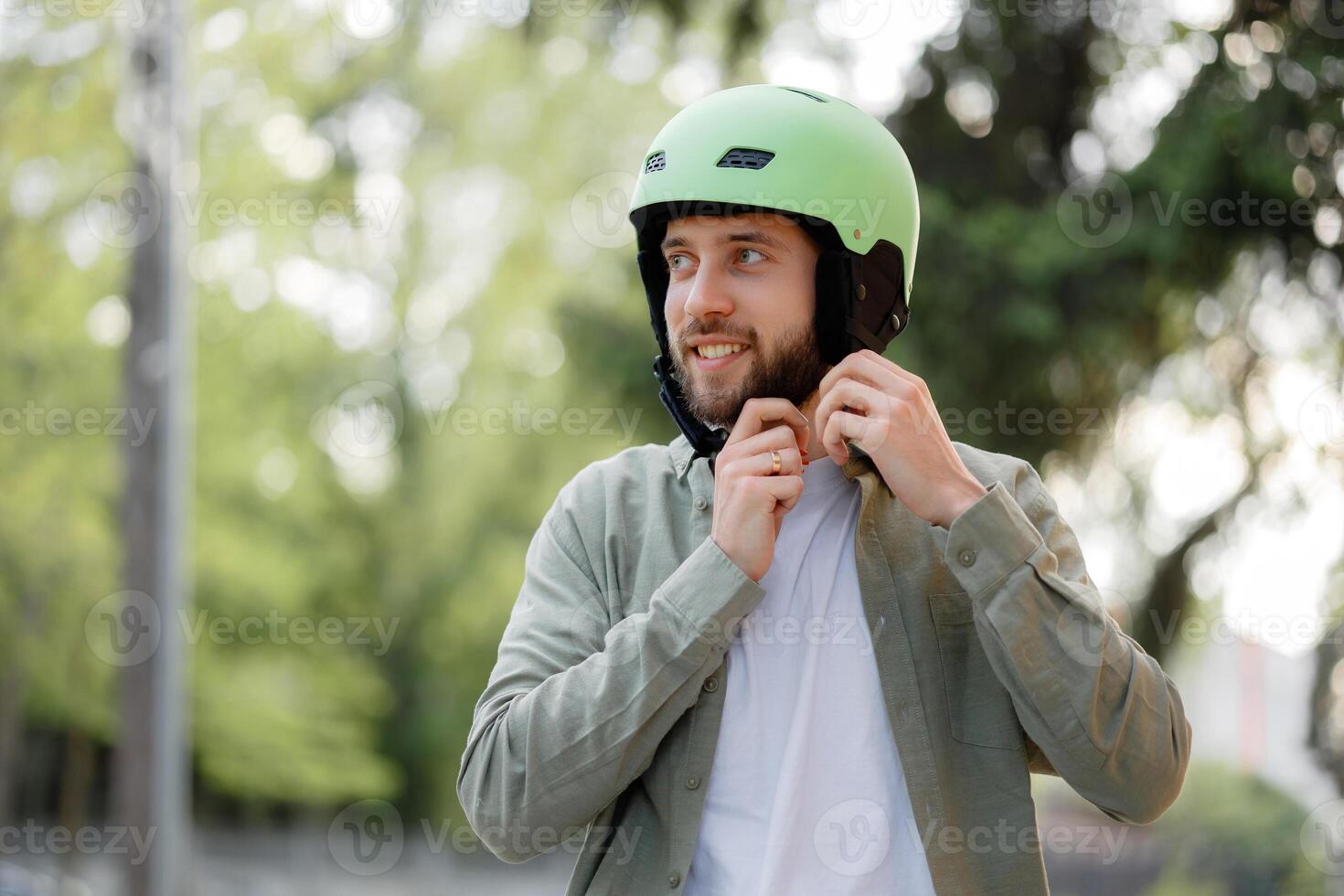 Young man prepares for cycling in park while smiling and wearing a green helmet during sunny afternoon photo
