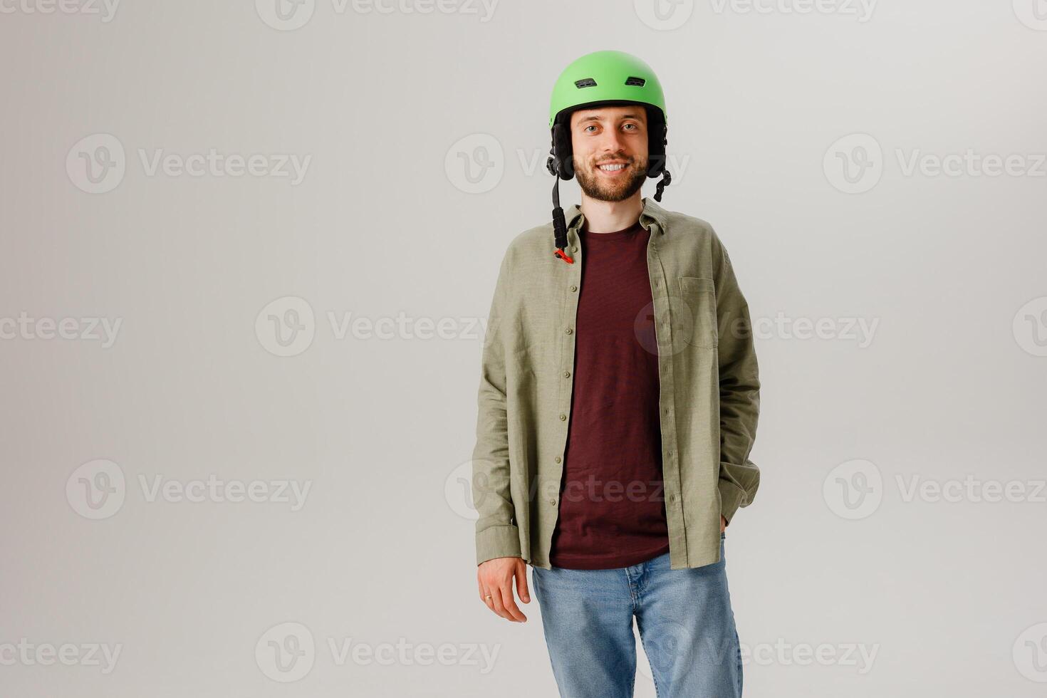 Young man in a green helmet stands confidently in a studio setting with a neutral backdrop, showcasing safety and style in casual attire photo