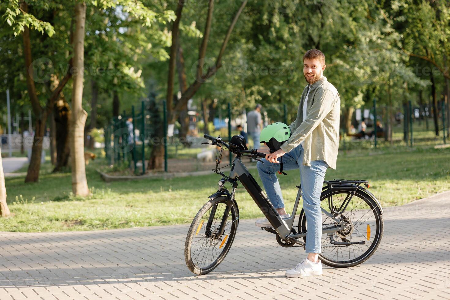 Man enjoys biking in a park on a sunny day while wearing a helmet and smiling at the camera photo