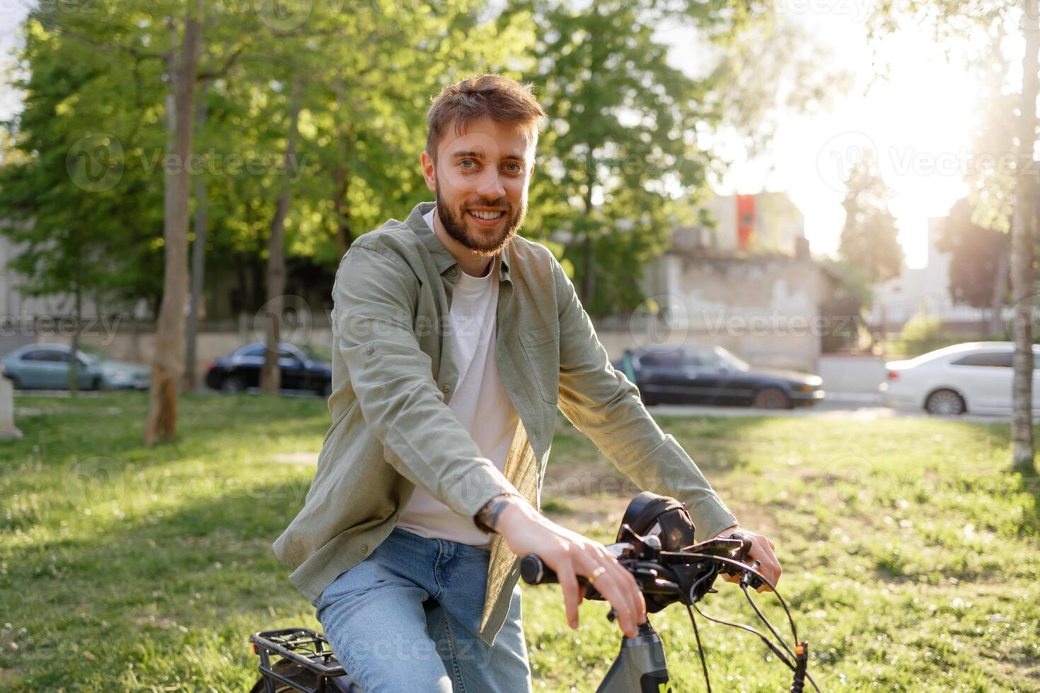 Young man enjoying a sunny day while biking in a park near urban surroundings and tall trees photo