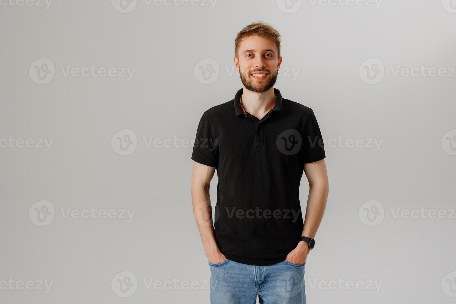 Young man smiles in casual black polo shirt and jeans against a neutral backdrop in a bright indoor setting photo