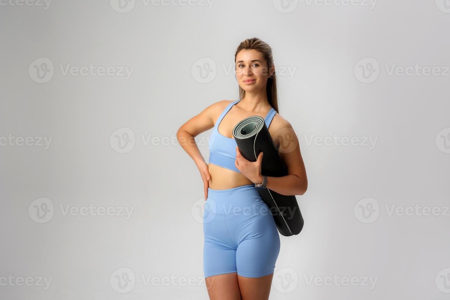 Yoga practitioner poses confidently with a mat, showcasing fitness and health lifestyle in a studio setting photo