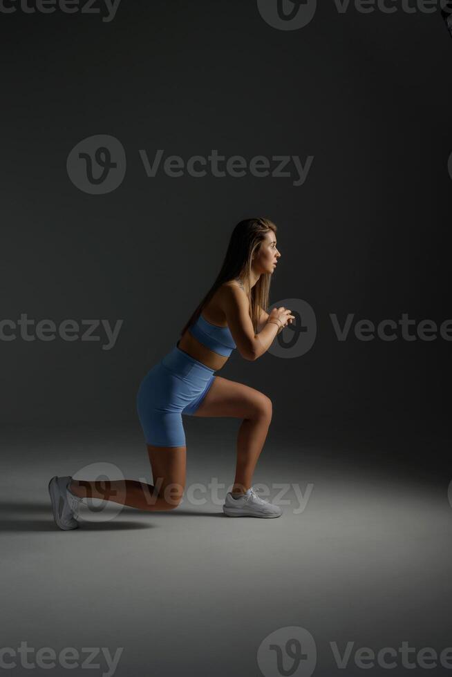 Fitness model performing a lunge exercise in a dimly lit studio showcasing strength and determination photo