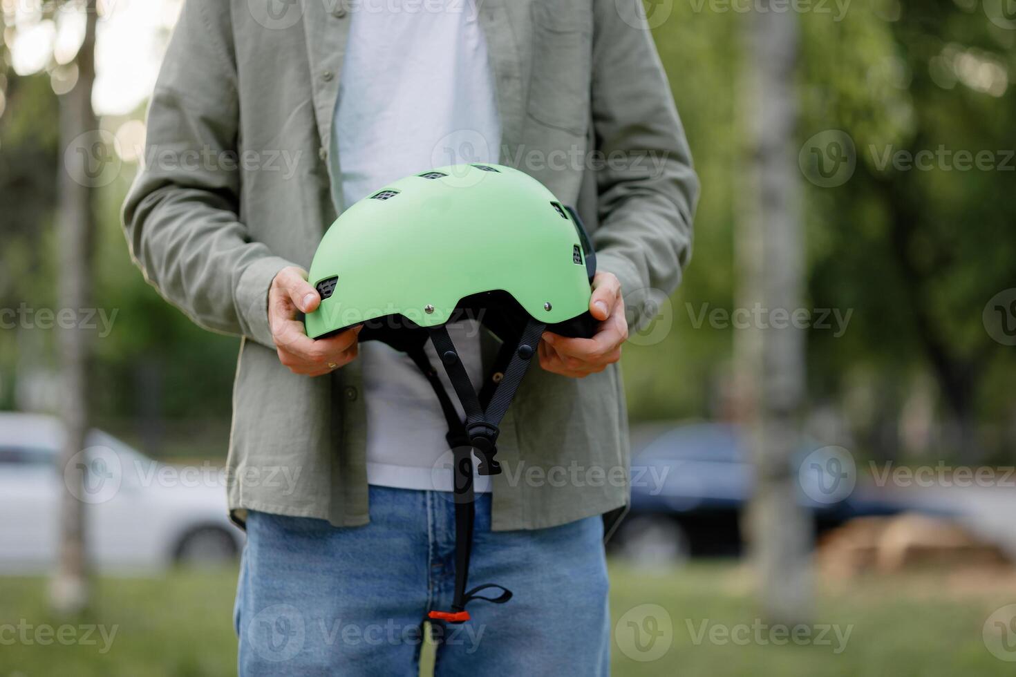 Person holding a green helmet in a park during the late afternoon near cars and trees photo