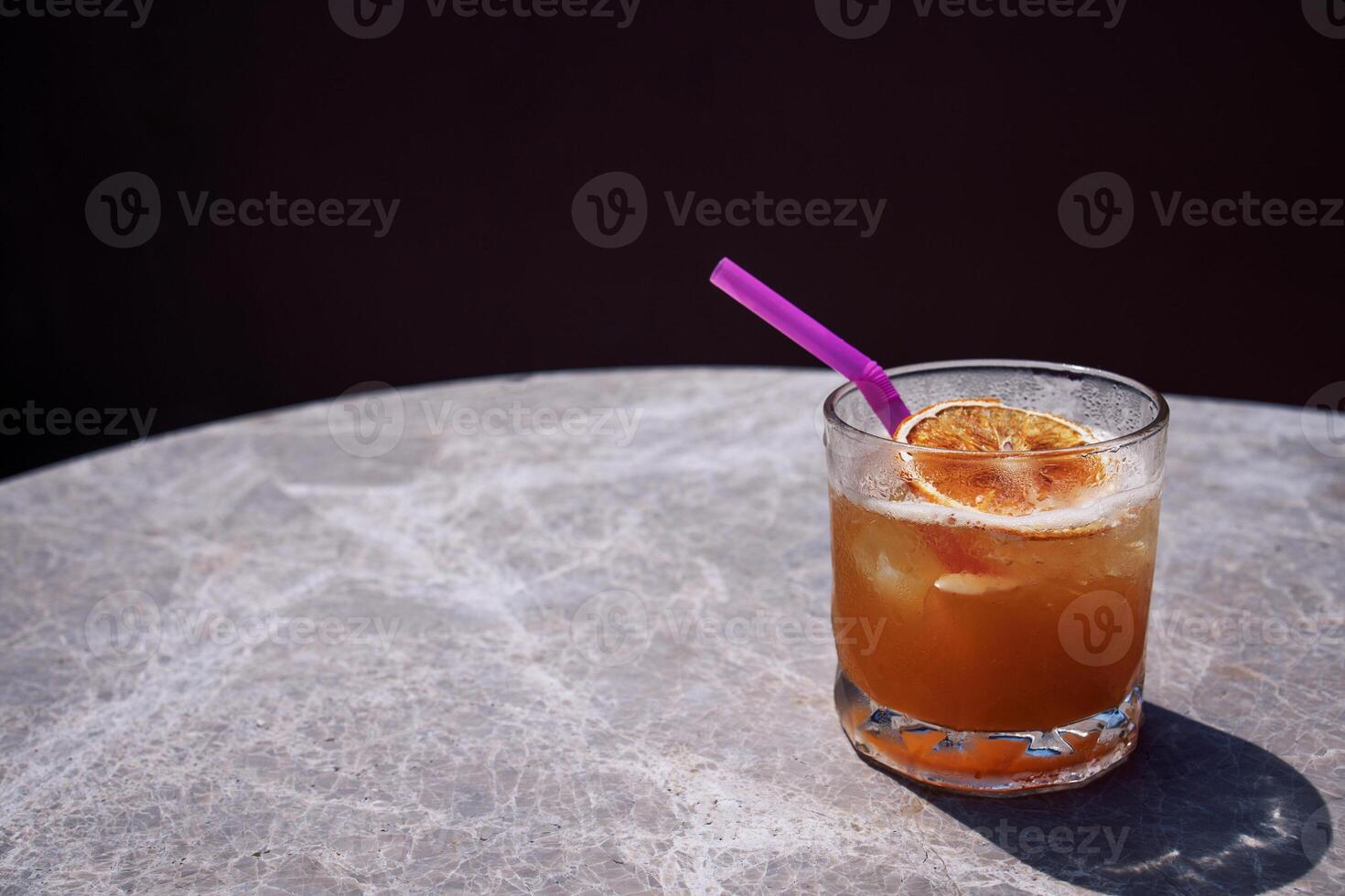 Close-up of a delicious citrus cocktail in a glass on a marble round table. A cup of carbonated drink with a straw and a slice of orange. photo
