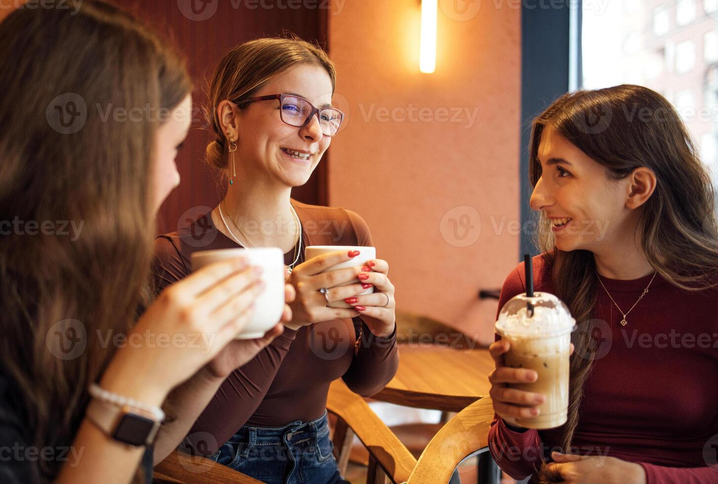 Young girls are laughing and drinking delicious coffee drinks in a cafe photo