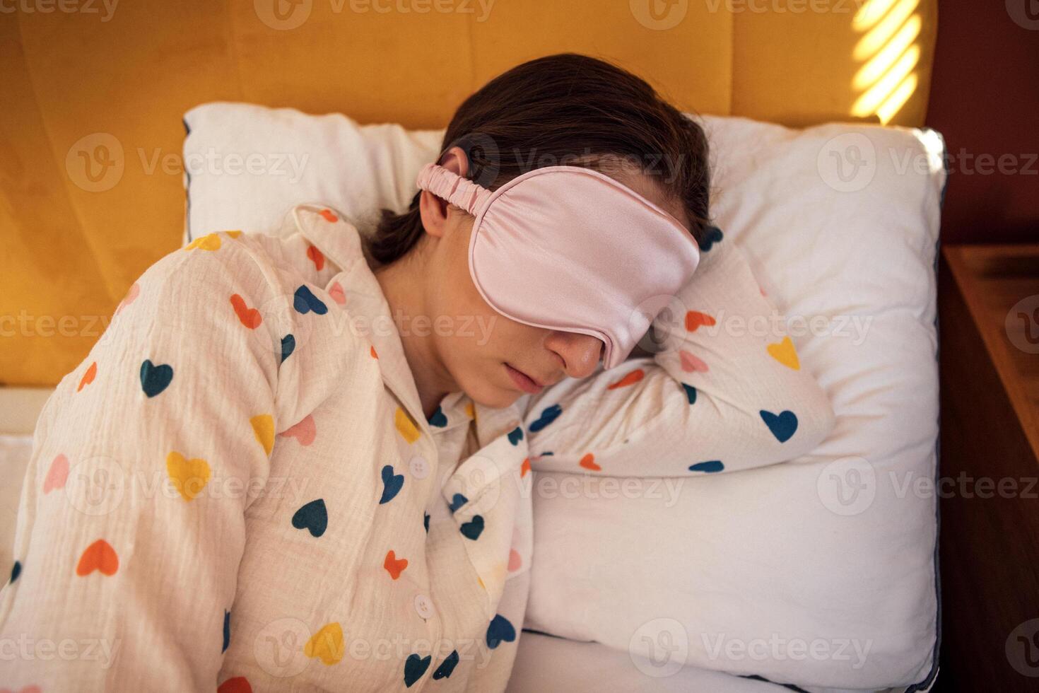 Close-up of a young woman in cute pajamas and a sleep mask lying in bed. The girl is sleeping peacefully on a pillow at home in the bedroom. photo