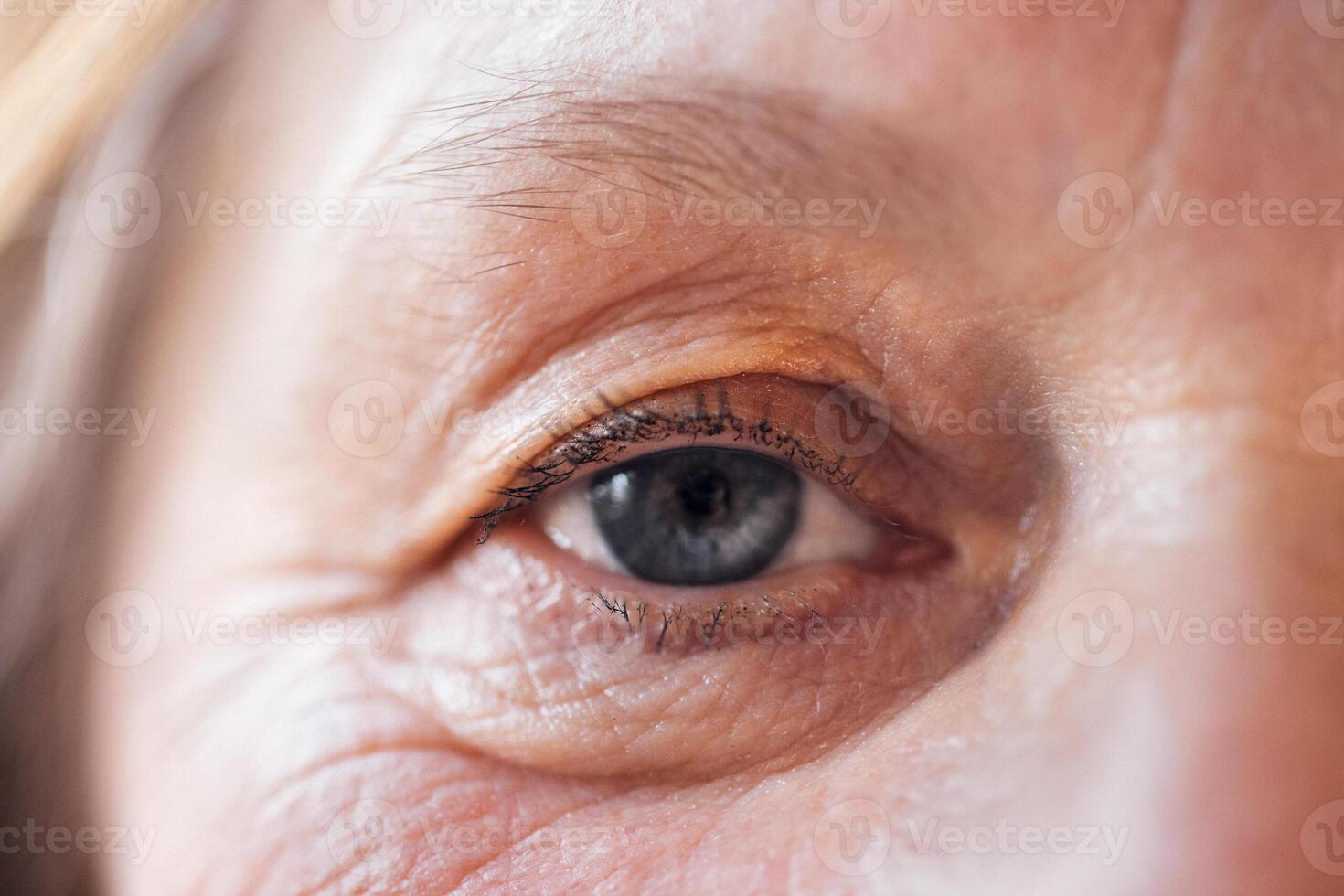 Close-up of an elderly woman blue eye. The face of a mature lady with facial wrinkles and no makeup. photo
