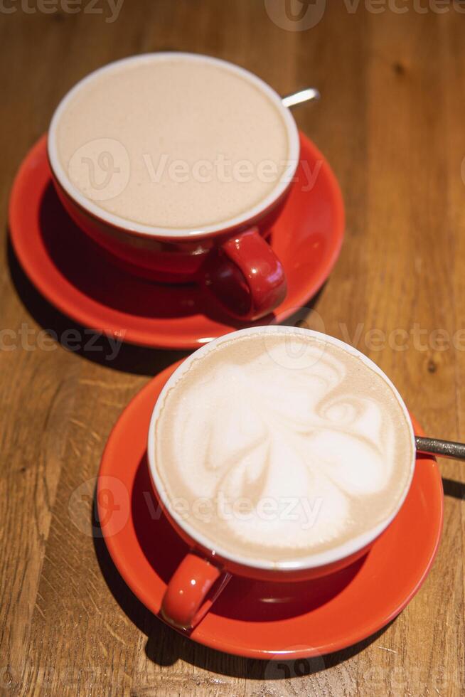 Cups of coffee in vibrant red ceramic mugs with intricate surface designs, resting on a smooth wooden table, evoking warmth and inviting sharing moment photo